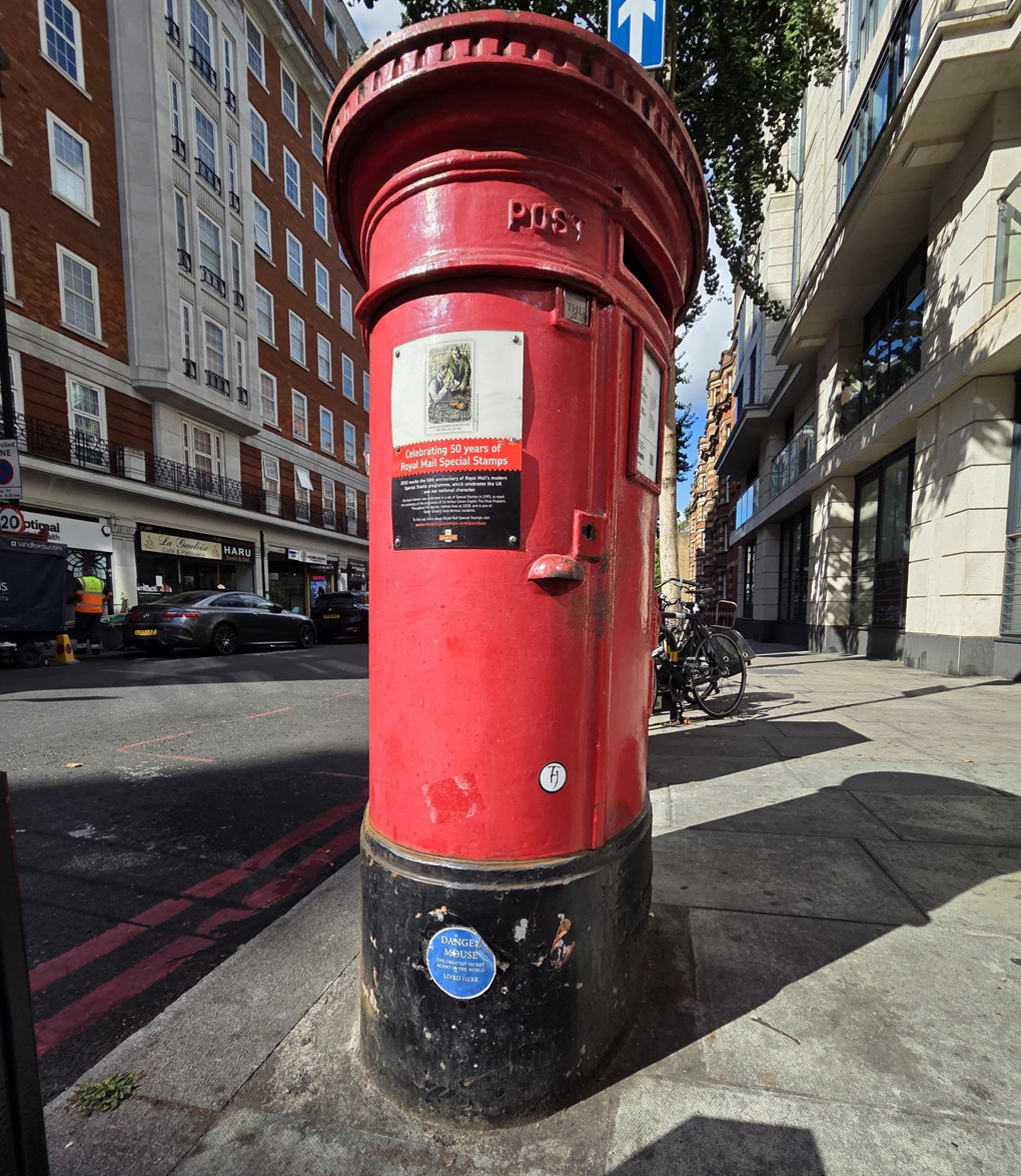 Red postbox with small blue plaque located on the black base