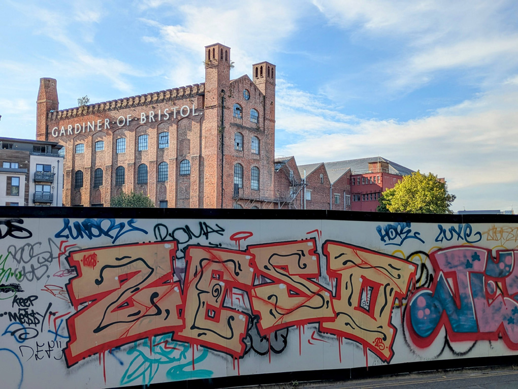 An old brick factory building in the background with a wall of graffiti in front.