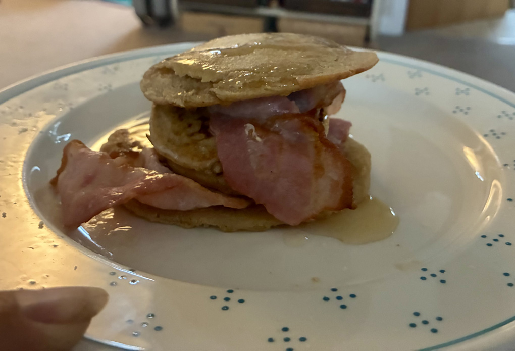 Drops gone pancakes, on a plate, layered with rashes of bacon and drizzled with maple syrup.