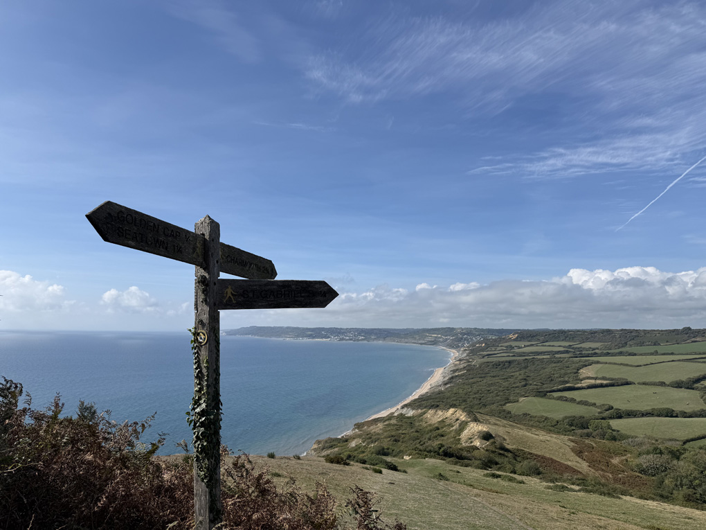 A finger post in the foreground and then a long sweep of Dorset coastline and sea