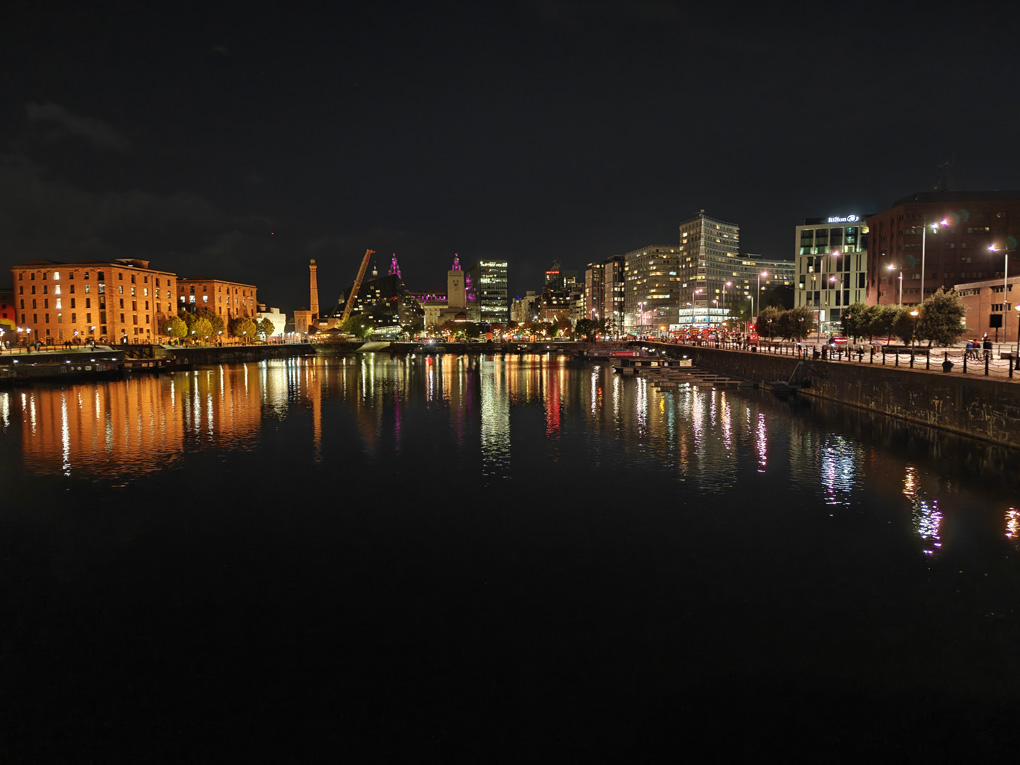 Distant illuminated buildings reflected in the dark waters of a dock, with the Liver Building in the centre.