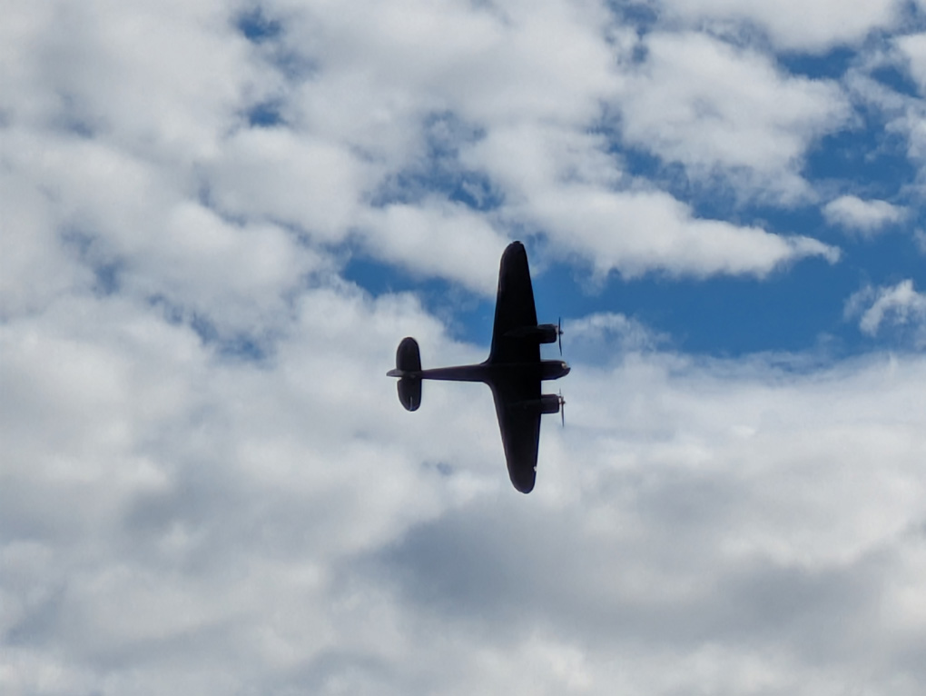 A twin engined WWII bomber silhouetted against a cloudy sky.