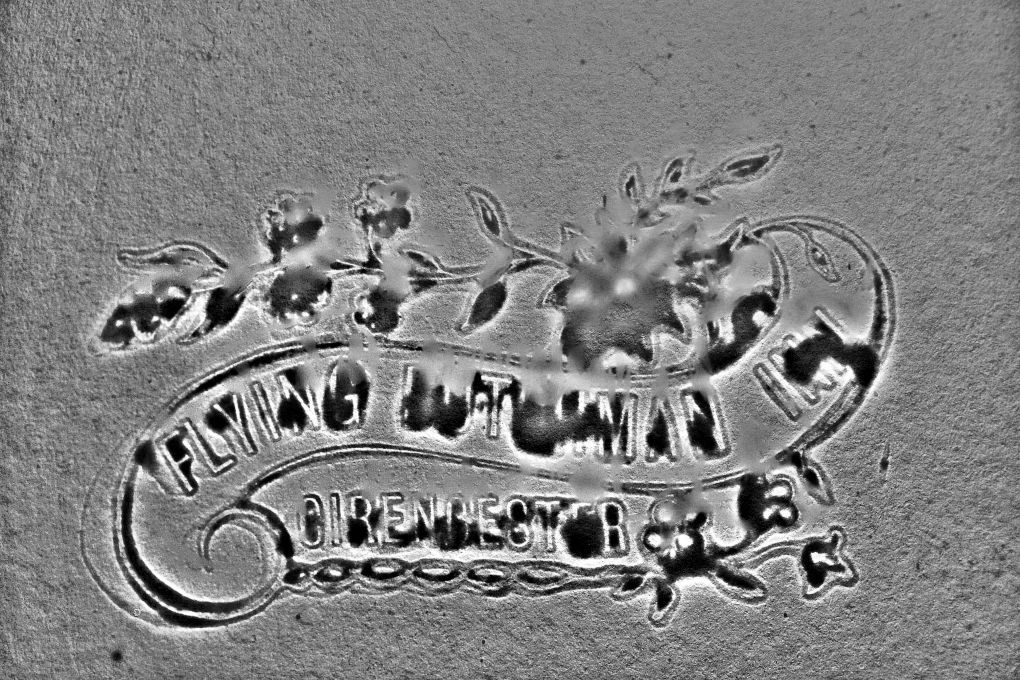 In monochrome, the etched lettering says 'The Flying Dutchman Inn' on one line, with 'Cirencester' on a second line. The scroll the text is around could be what led the author to think it was a ship.