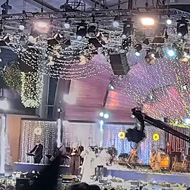 An outdoor stage at night with a large crowd in attendance with a large soundsystem, screen and musicians on stage.