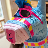 Pinata shaped like a llama wearing sunglasses, with girl in background.