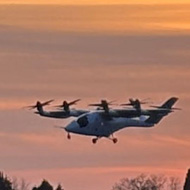 Against a sunset backdrop a four prop, chubby aircraft can be seen maintaining a  fixed height just above the runway.