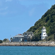 View from Island Bay, Wellington. Looking out over the sea as the coast curves around. Bench in foreground. Hills and lighthouse in distance.