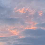 A cloudy sky obscures a deep orange and purple sunset above a green park