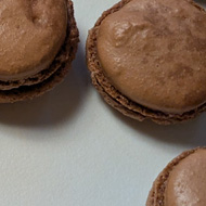 About twenty chocolate macarons cooling on a board having just come out of the oven