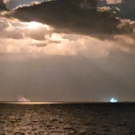 Low cloud over a body of water, bright light emitting from center caused by the burners from a rocket launch