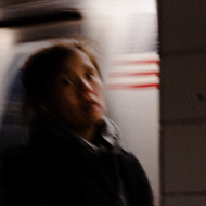 A slightly blurred photo of a woman walking along a subway platform in new york with the train moving behind her