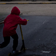 On a small side street in Ieper, a child in a red hoodie rides off on his scooter past the red brick walls and under a bright blue sky