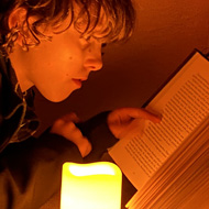 A boy reading a book by candlelight