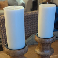 Two wooden candlesticks with round white candles, standing on a wooden table.