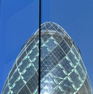 The famous “Gherkin” building and much older stone building reflected in an other glass building. Showing the different eras of London architecture