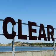 Sunny day in a hot country. On top of a dam is a huge sign in mental reading “on a clear day you can see forever “