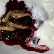 Three small round pancakes stacked on a plate with blue berry compote and white younger oozing from between the layers and all over the top.