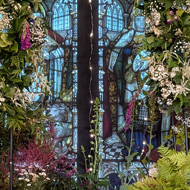 A beautiful woodland scene created with flowers and greenery around a stained glass window.