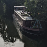 View over the river in the evening sun, a canal boat moored on one side and trees lining the banks