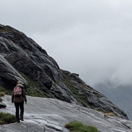 A small figure is walking ahead up on the ancient weathered rock that rises beside Loch Coruisk on grey day with low cloud enveloping the peaks of the steep hills around