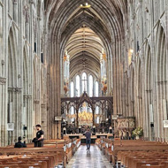 View inside a grand cathedral with soaring stone arches, vaulted ceiling leading to an alter in the distance and rows of wooden chairs