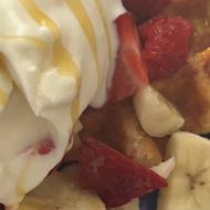 A pile of sugar waffles, fresh fruit, Greek yoghurt and honey on a bright blue plate