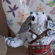 A DnD bear figurine mid roar, standing next to a candle, with a pretty floral plate displayed in the background.