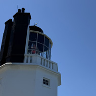 A large white lighthouse in the foreground with blue sea and sky in the background