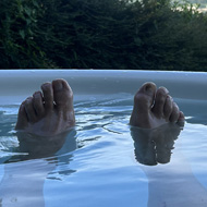 View from a hot tub with sunny hills in distance. Two legs floating on surface of the water from the person taking the photos and enjoying the coolness.