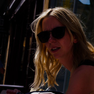Woman in a black sundress pushing a stroller reaches back for her toddler’s hand. Between the toddler and the mother is a branching crack in the sidewalk