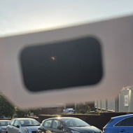A cheap looking pair of cardboard glasses with black film lenses is held up to the sky. Through one of the lenses you can see the sun almost completely hidden by the moon