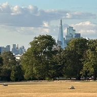 View over London from Ruskin Park with brown grass. Shard and other London buildings in distance.