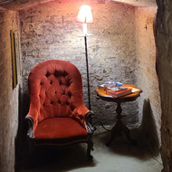 A red chair with a lamp to the right, in a brick alcove. A sign above reads - Spooky book nook. The proprietor dares you to read for 5 minutes within.