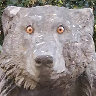 A sculpture of the top half of a bear, overlooking a high wall