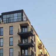 A park surrounded by beige apartment blocks with yellow grass and people stood or sat around looking at the sun