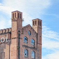 An old brick factory building in the background with a wall of graffiti in front.
