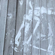 Dirty white wooden doors with a horse's outline drawn into the grime, beside a French 'Terrain Militaire' warning sign.