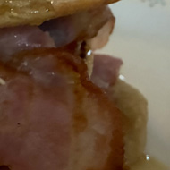 Drops gone pancakes, on a plate, layered with rashes of bacon and drizzled with maple syrup.