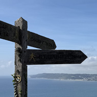 A finger post in the foreground and then a long sweep of Dorset coastline and sea