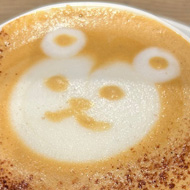 Picture of a milky coffee with the image of a cartoon bear fashioned out of the foam and froth on top of the mug.