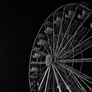 A motionless ferris wheel in the dead of night at the Weymouth seaside. It looks like a white skeleton against the night sky, looming overhead.