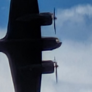 A twin engined WWII bomber silhouetted against a cloudy sky.